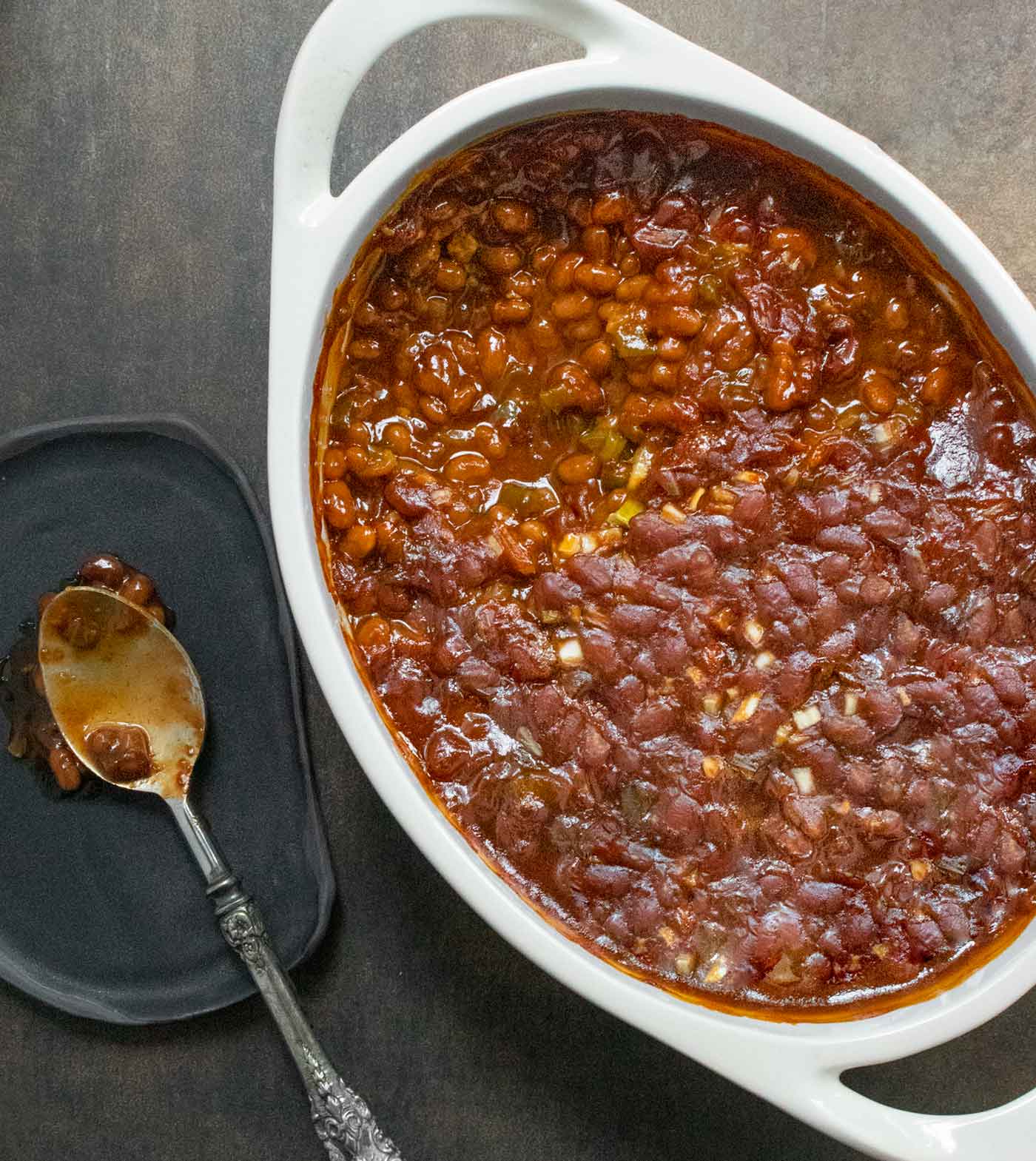 Overhead shot of the baked beans in a white baking dish with a spoon on the side.