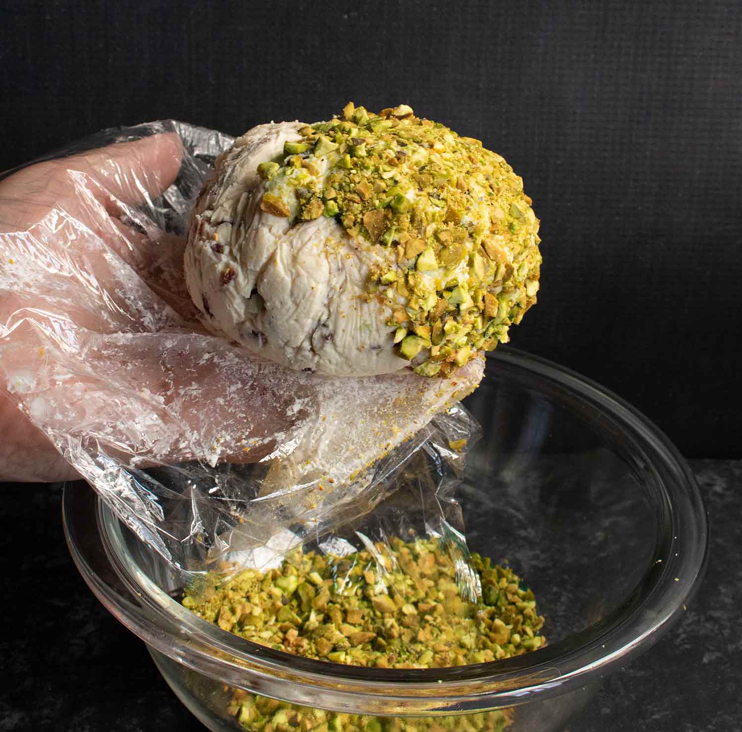 Covering the cheese ball with a pistachio coating.