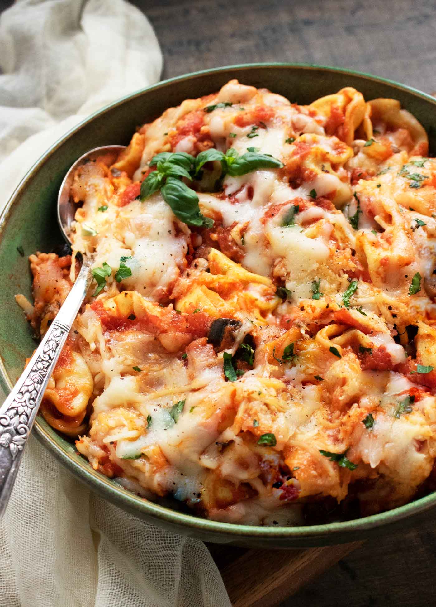 Side-angled, close-up view of a Pizza Tortellini in a green bowl with a spoon.