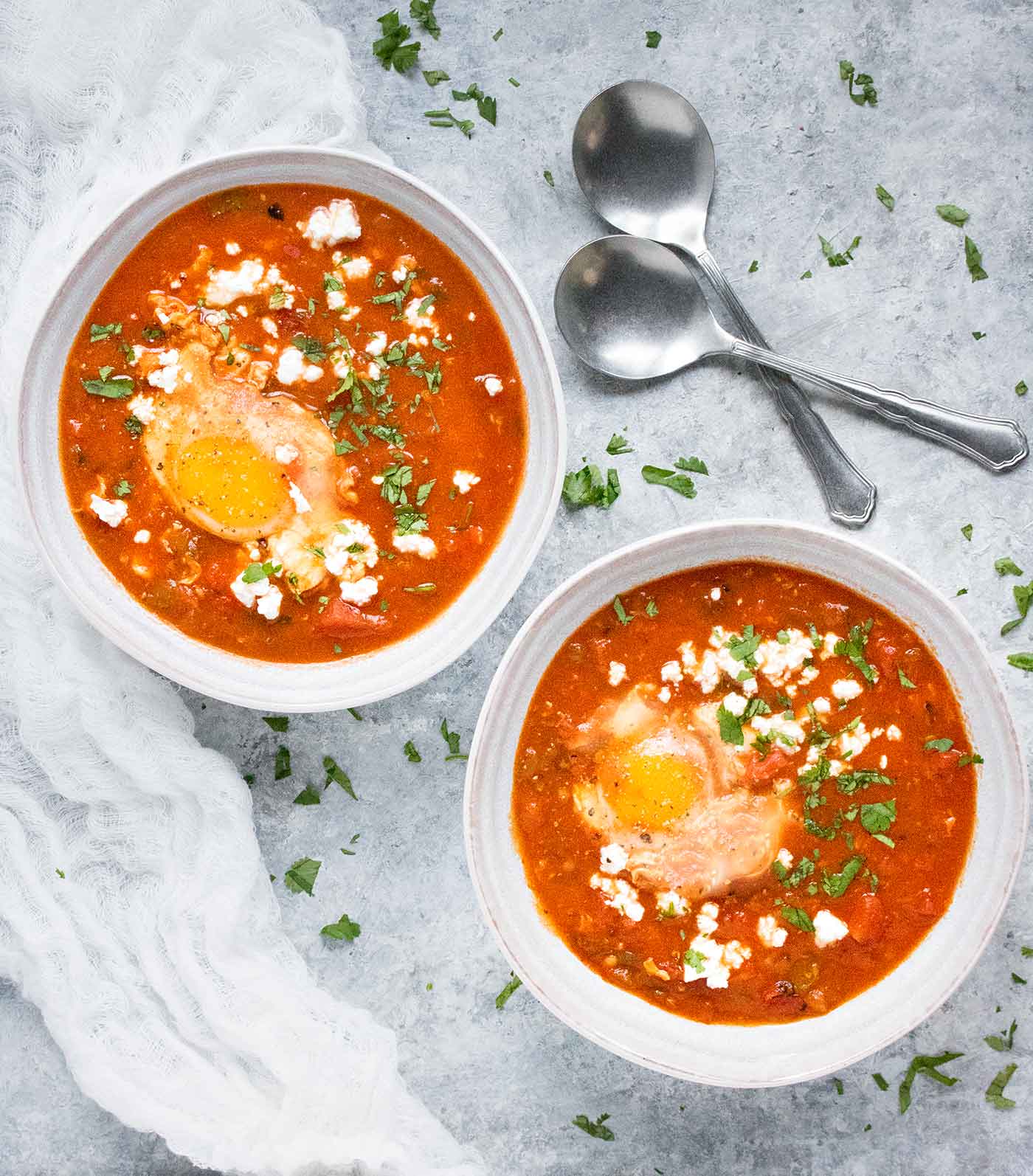 Two bowls of Shakshuka Soup topped with an egg and cheese