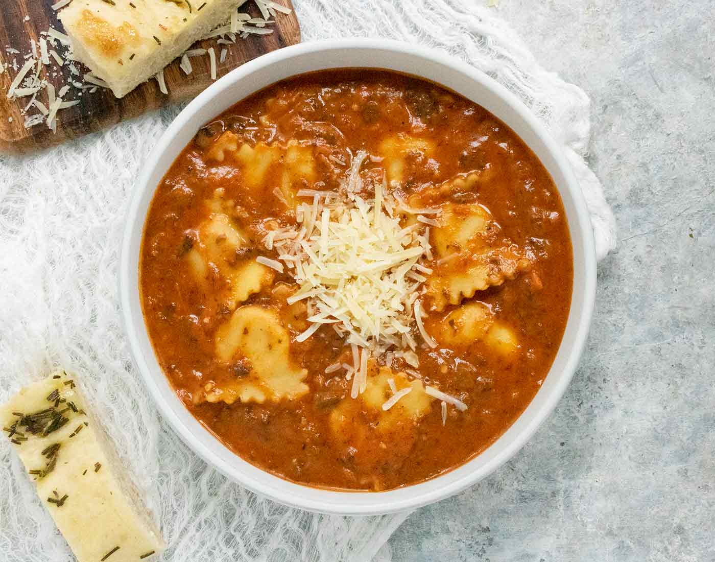 Ravioli soup in a white bowl with a side of bread.