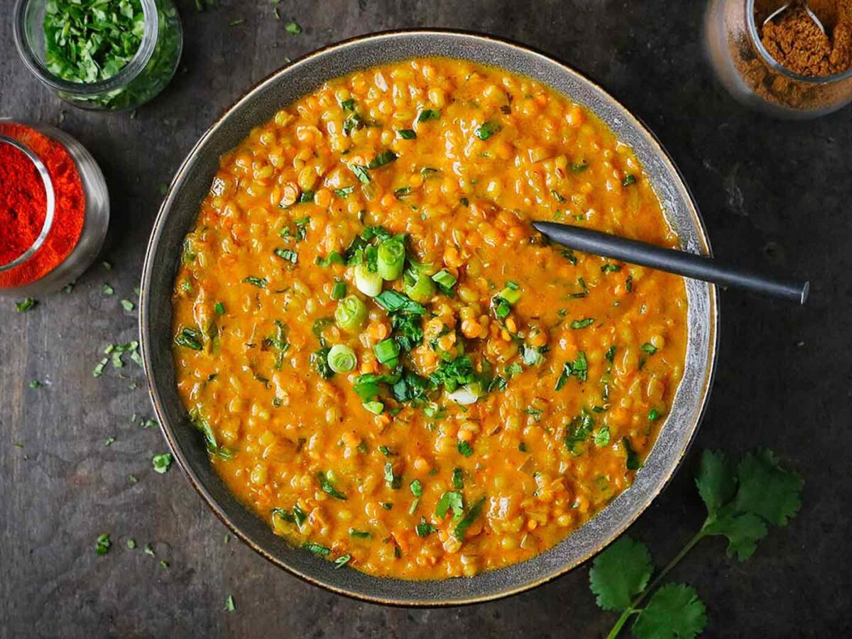 Overhead view of Red Lentil Masala Soup in a dark gray bowl with a rustic spoon.