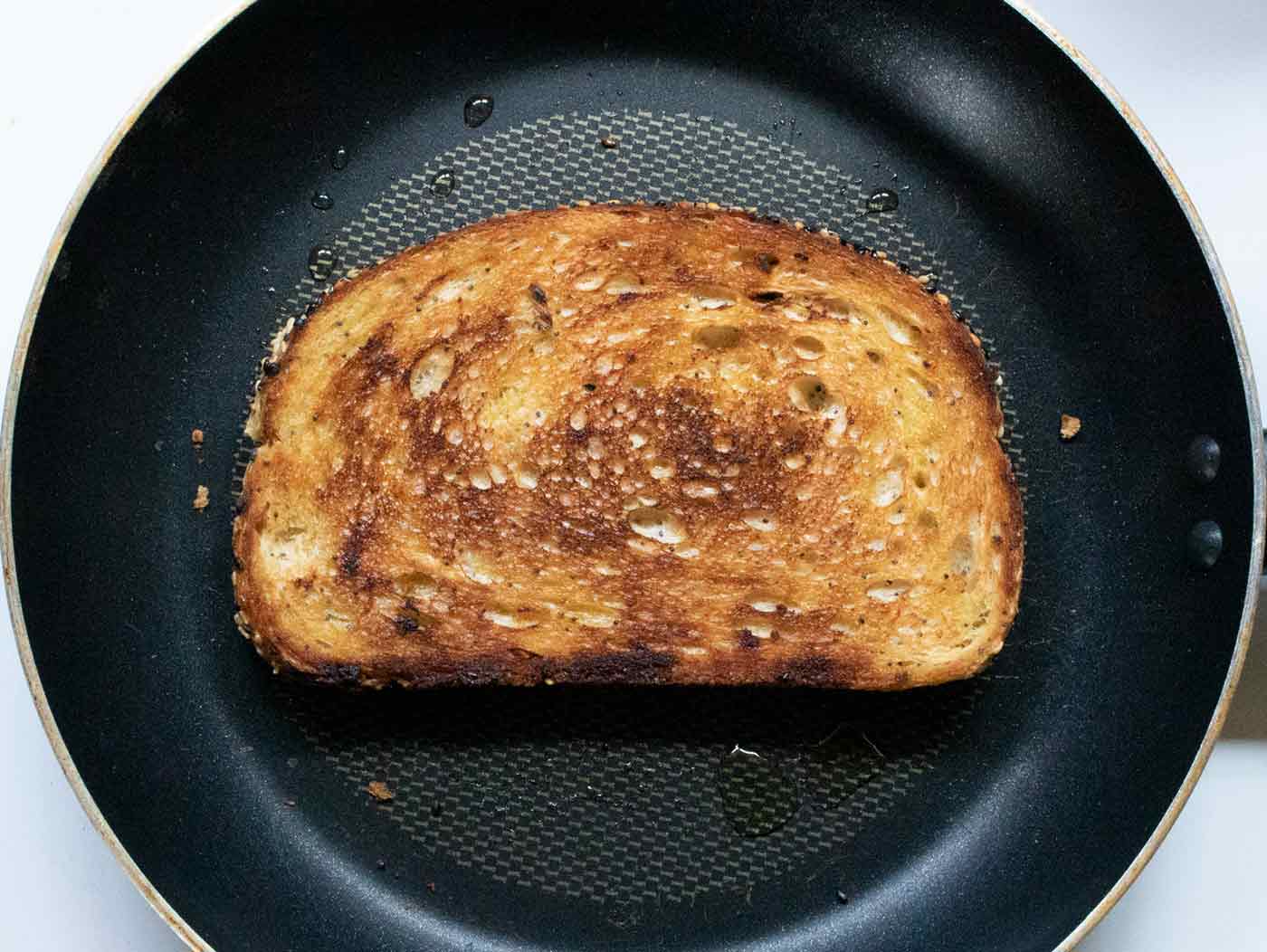 Slice of marble rye bread frying in some olive oil in a skillet.