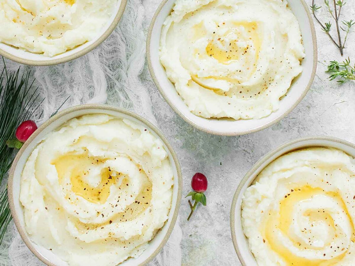 Four individual servings of roasted garlic mashed. potatoes in small bowls.