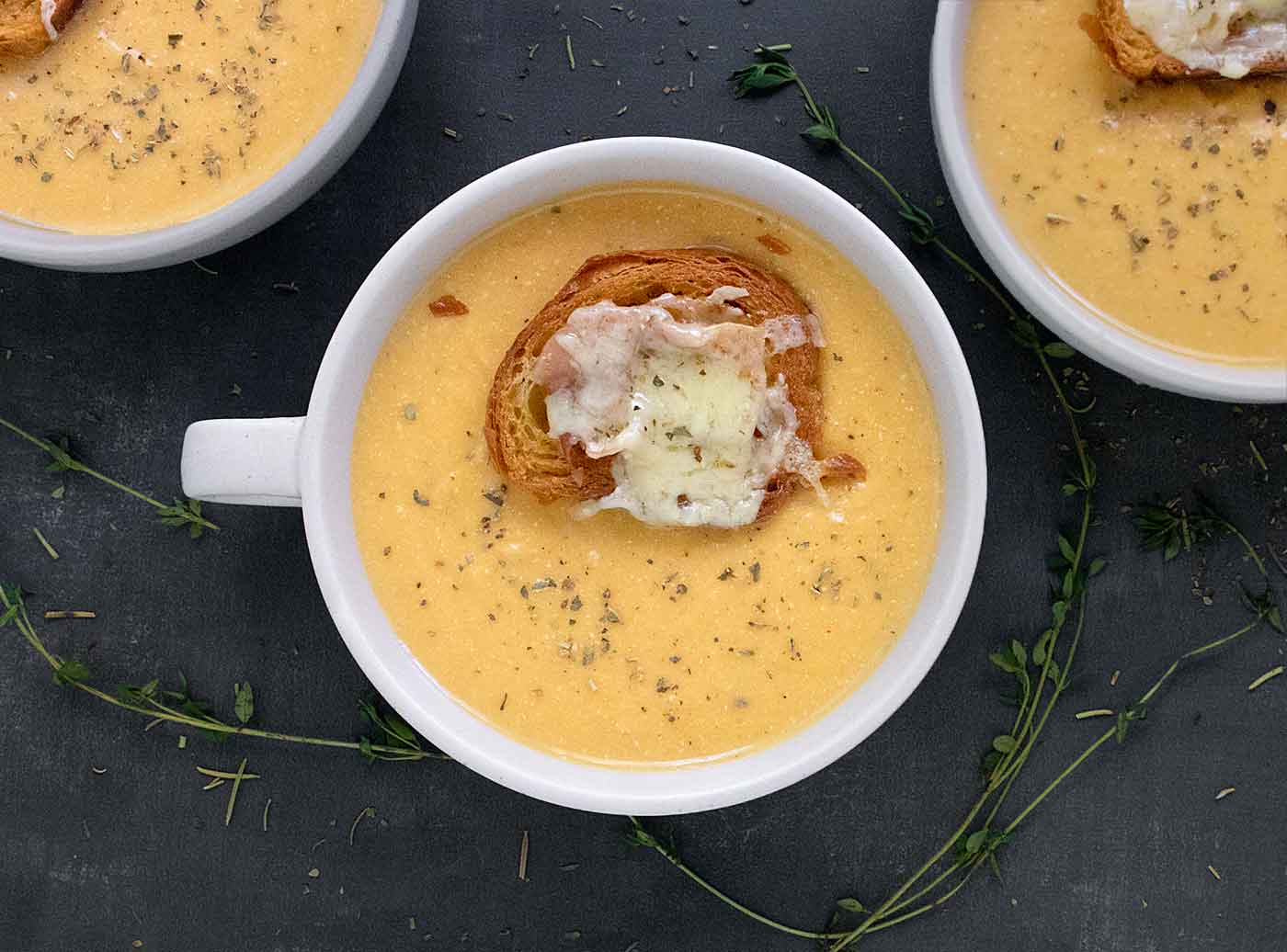 Overhead view of one bowl and two partial bowls of Roasted Winter Squash and Feta Soup, topped with croissant croutons.