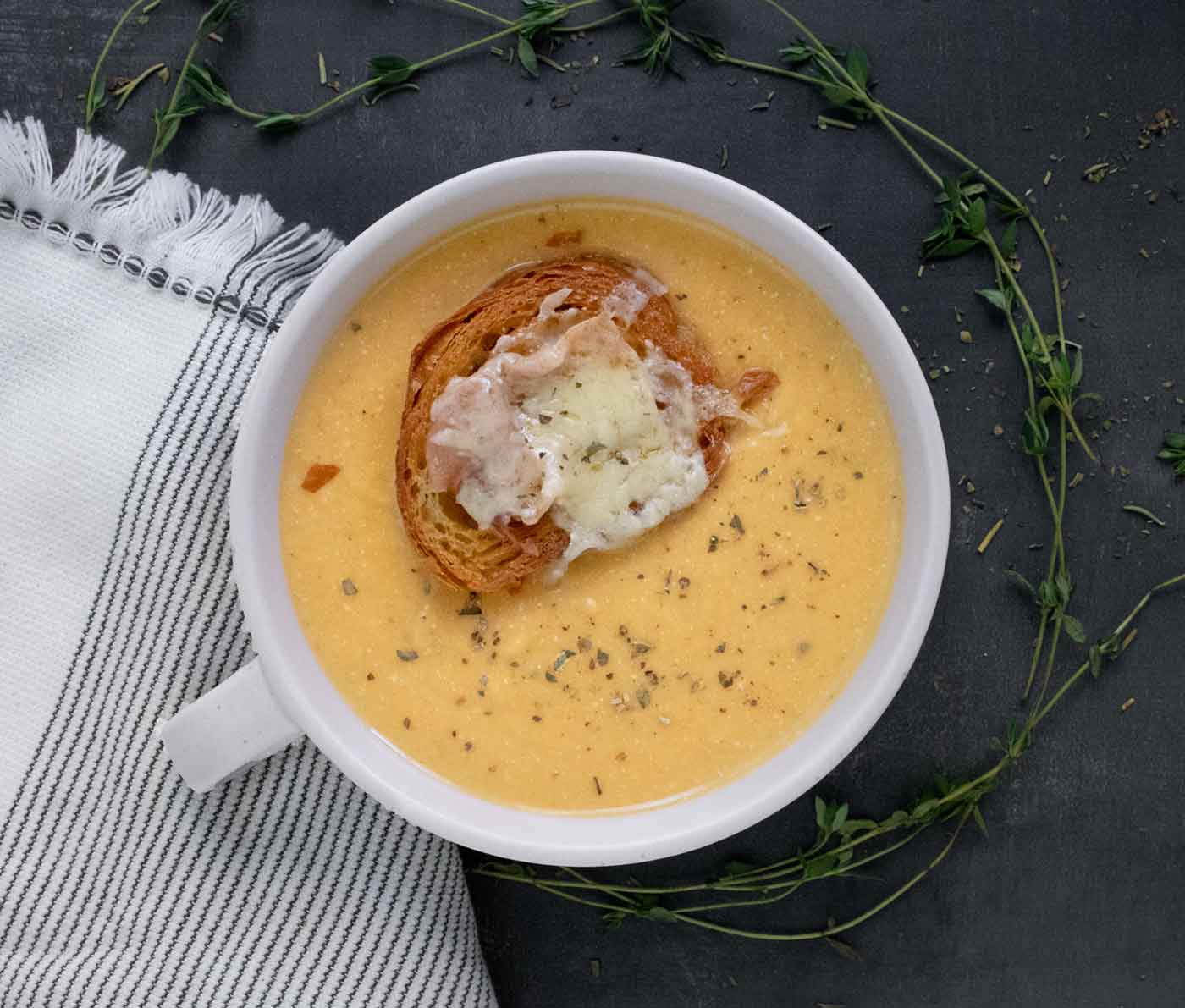 Overhead view of a bowl of Roasted Winter Squash and Feta Soup, topped with a Crossiant crouton with prosciutto and cheese.