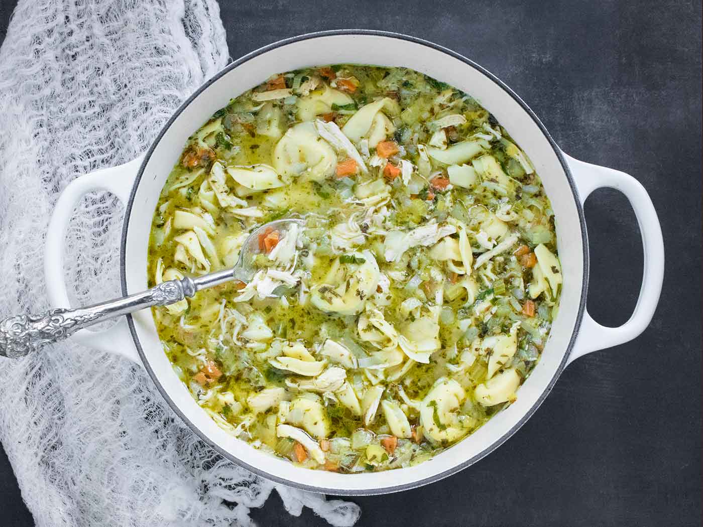 Rotisserie Chicken Tortellini Soup in a white Dutch oven, with a serving spoon.