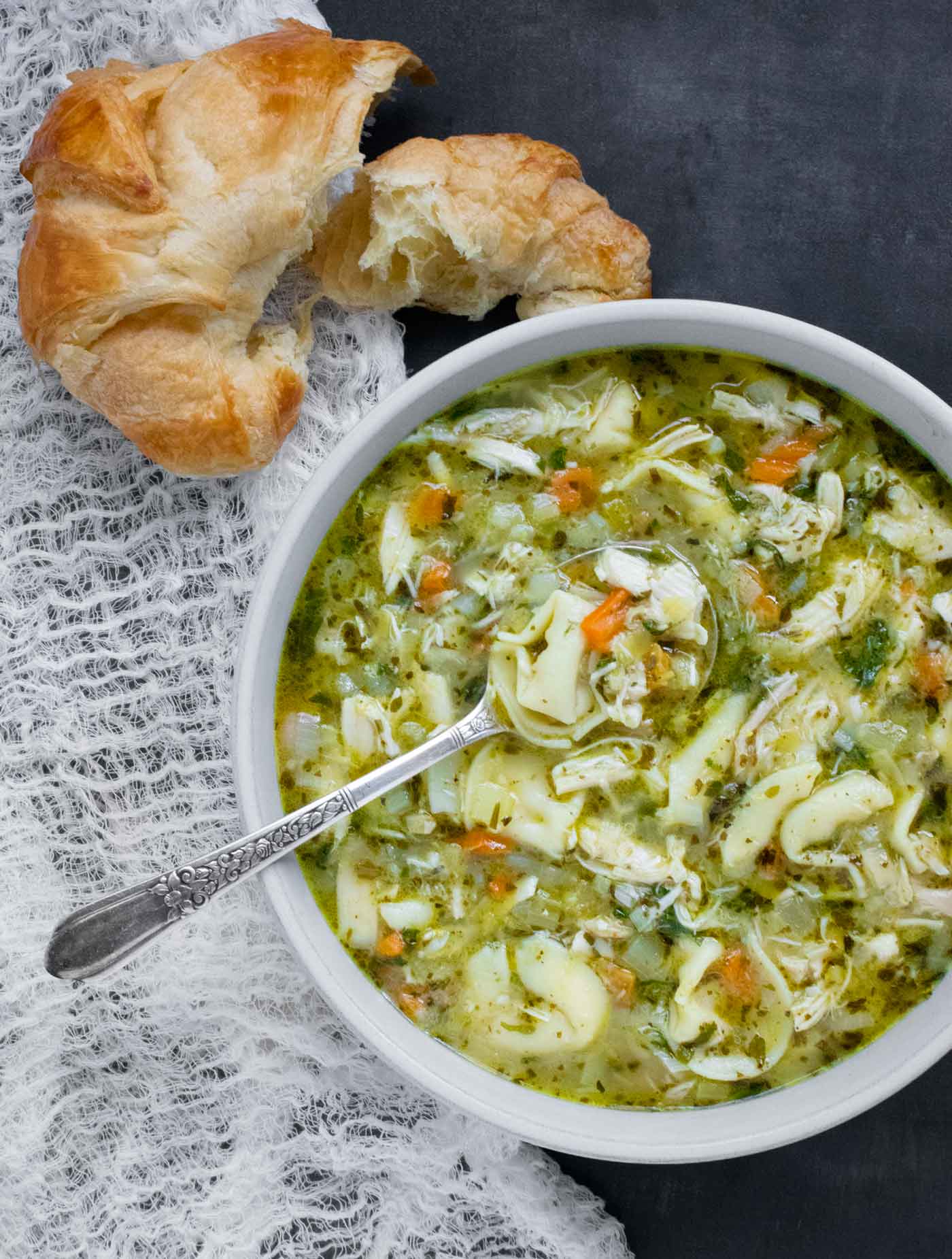 Overhead view of Rotisserie Chicken Tortellini Soup with a croissant on the side.