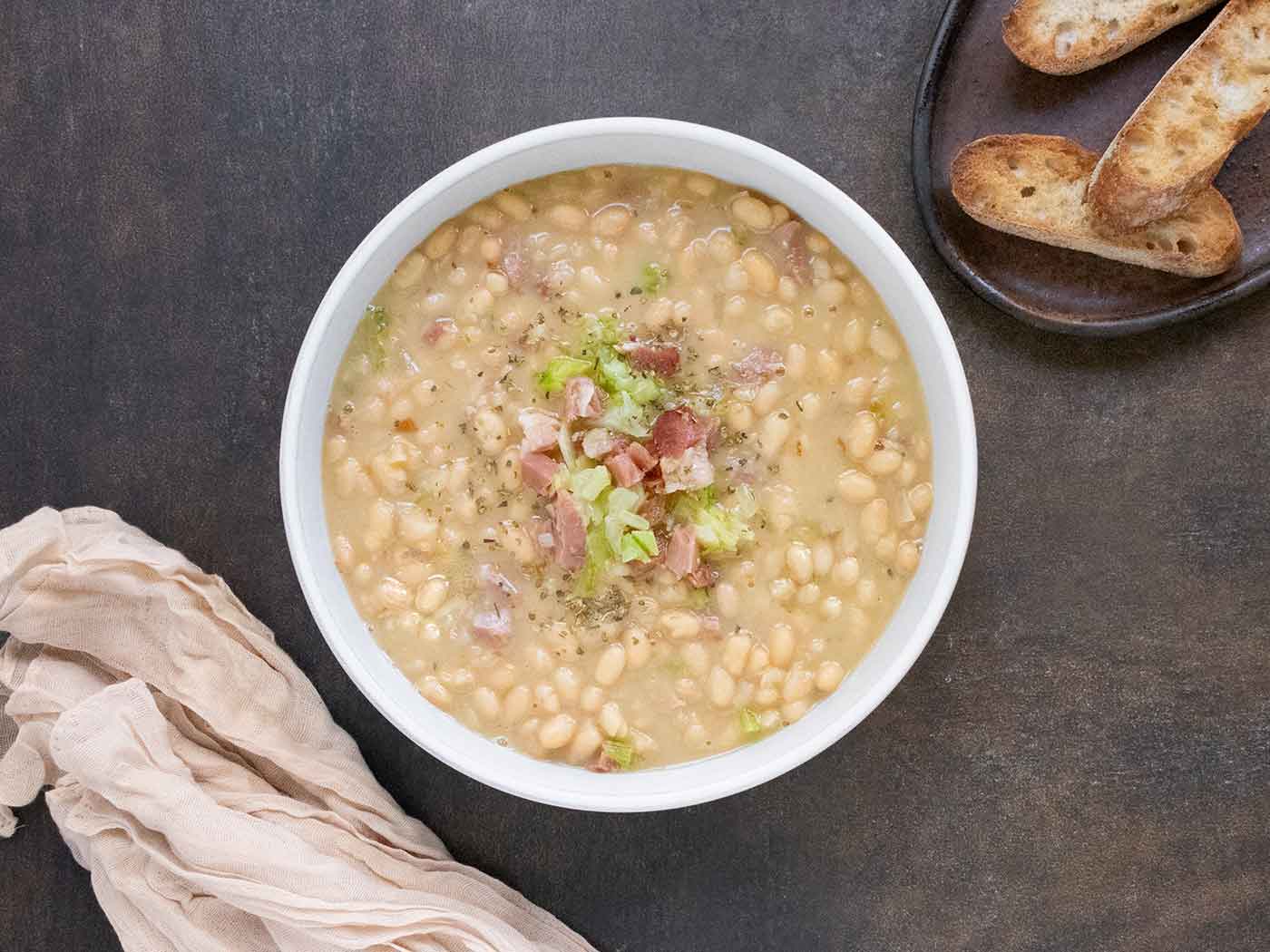 An overhead view of Senate Bean Soup in a white bowl with a side of bread.