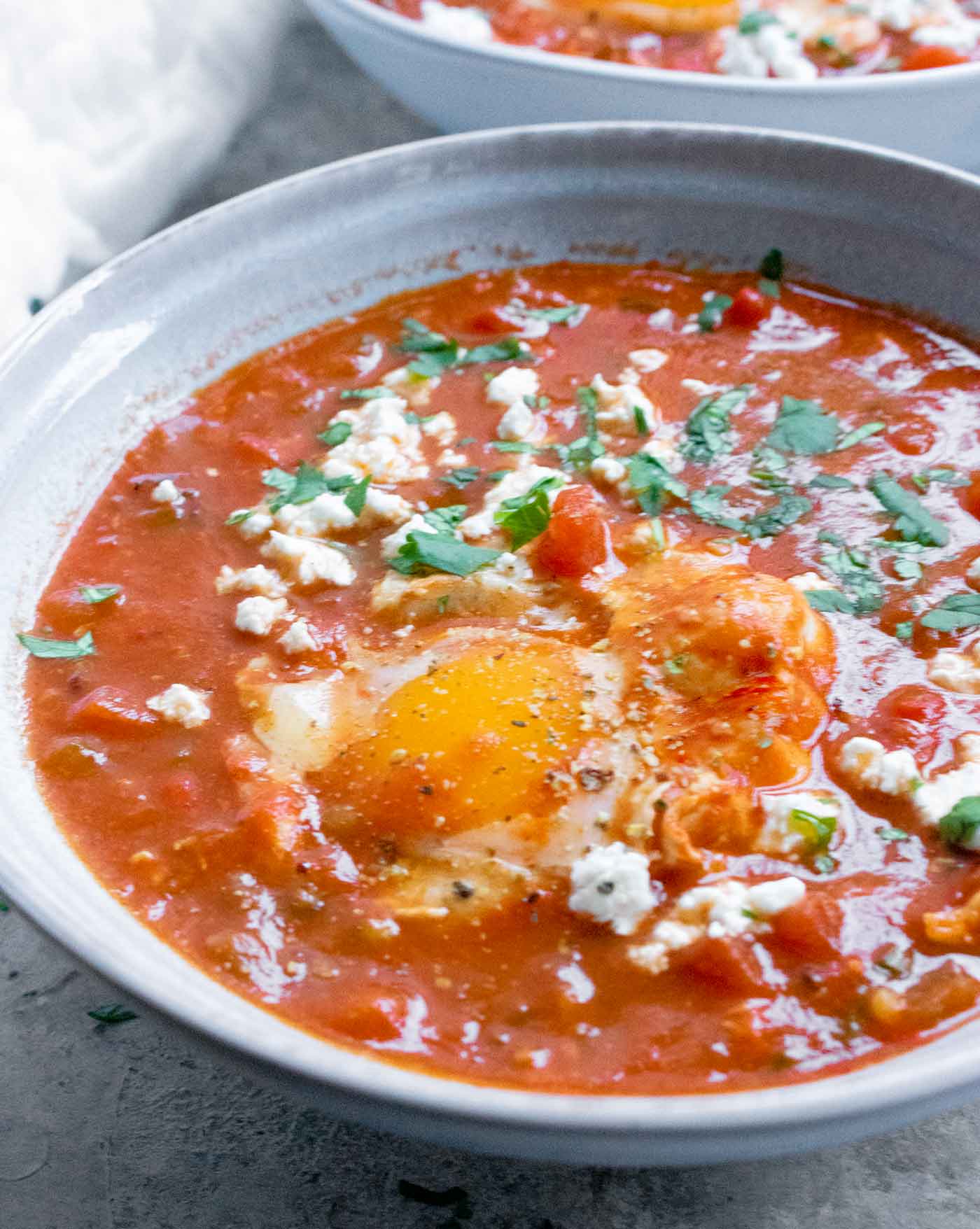 Side angle view of Shakshuka Soup in a light blue bowl, topped with an egg.