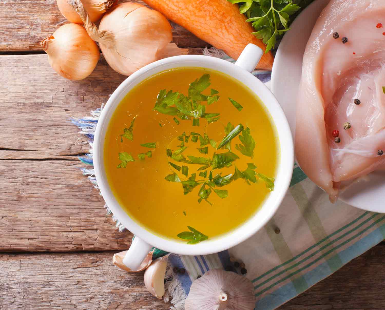 Soup stock in a white bowl on a wooden table.