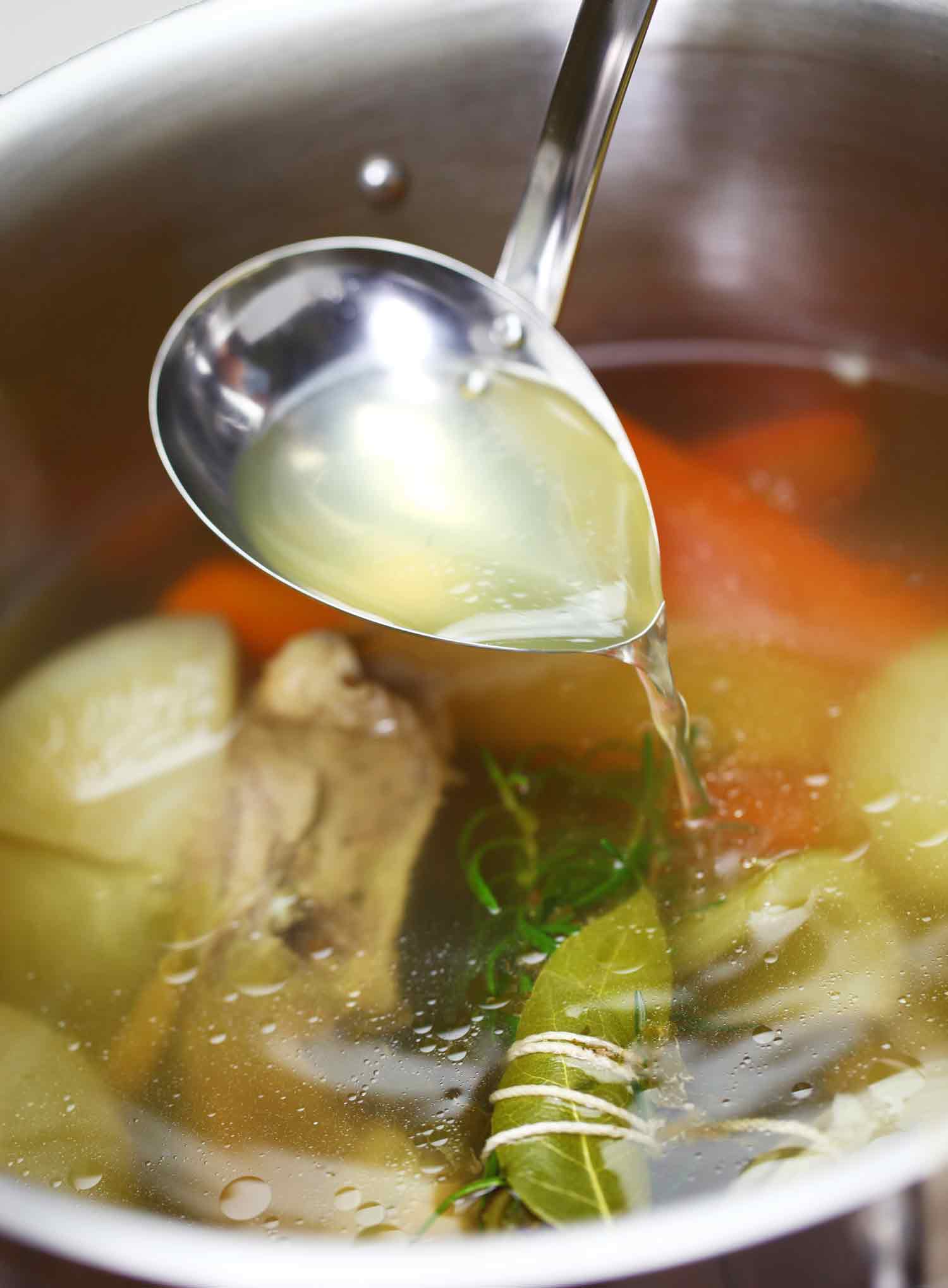 A pot of chicken stock with a ladle pouring liquid back into the pot.