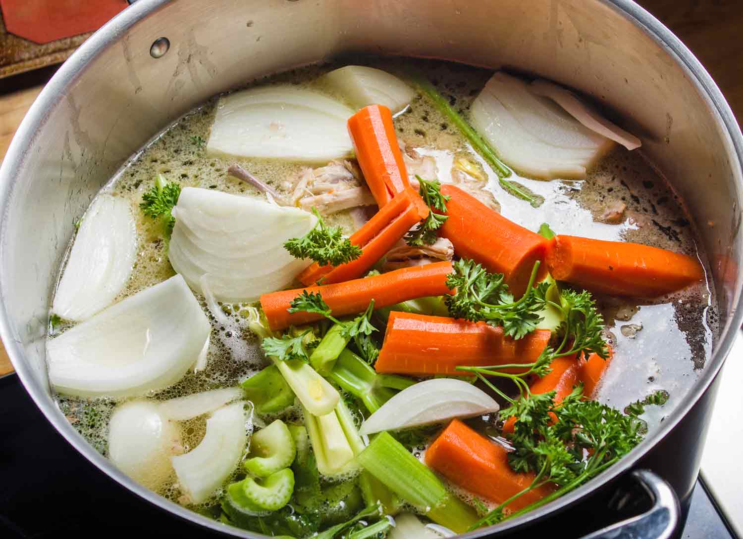 A stock pot filled with vegetables, chicken and water for making soup stock.