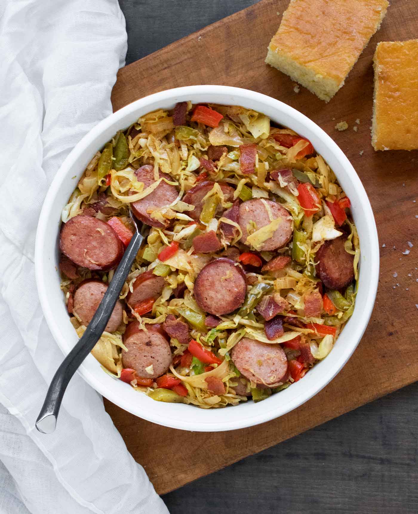 A bowl of Southern Fried Cabbage in a bowl with a fork on a wooden cutting board, with cornbread on the side.