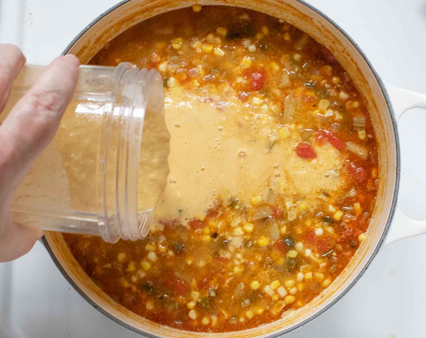Adding the blended cups of soup, plus dairy and lime juice, back into the soup to thicken it up.