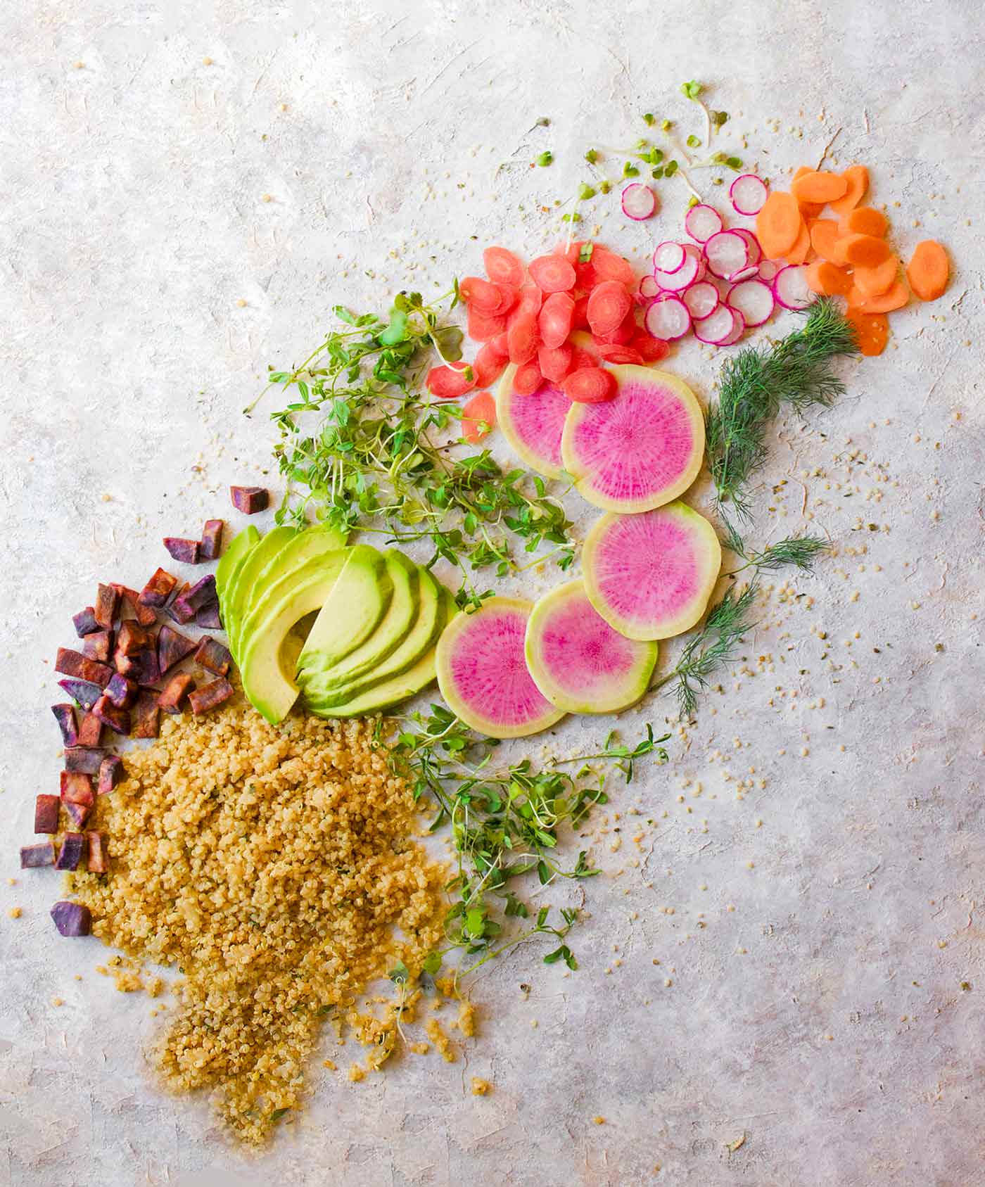 Ingredients for a vegan buddha bowl, spread across a table in a rainbow