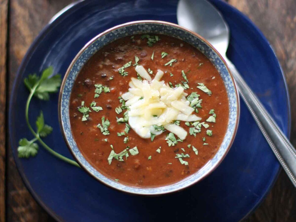 Sriracha Black Bean Soup in a flowery blue and white soup bowl on a medium blue charger plate.