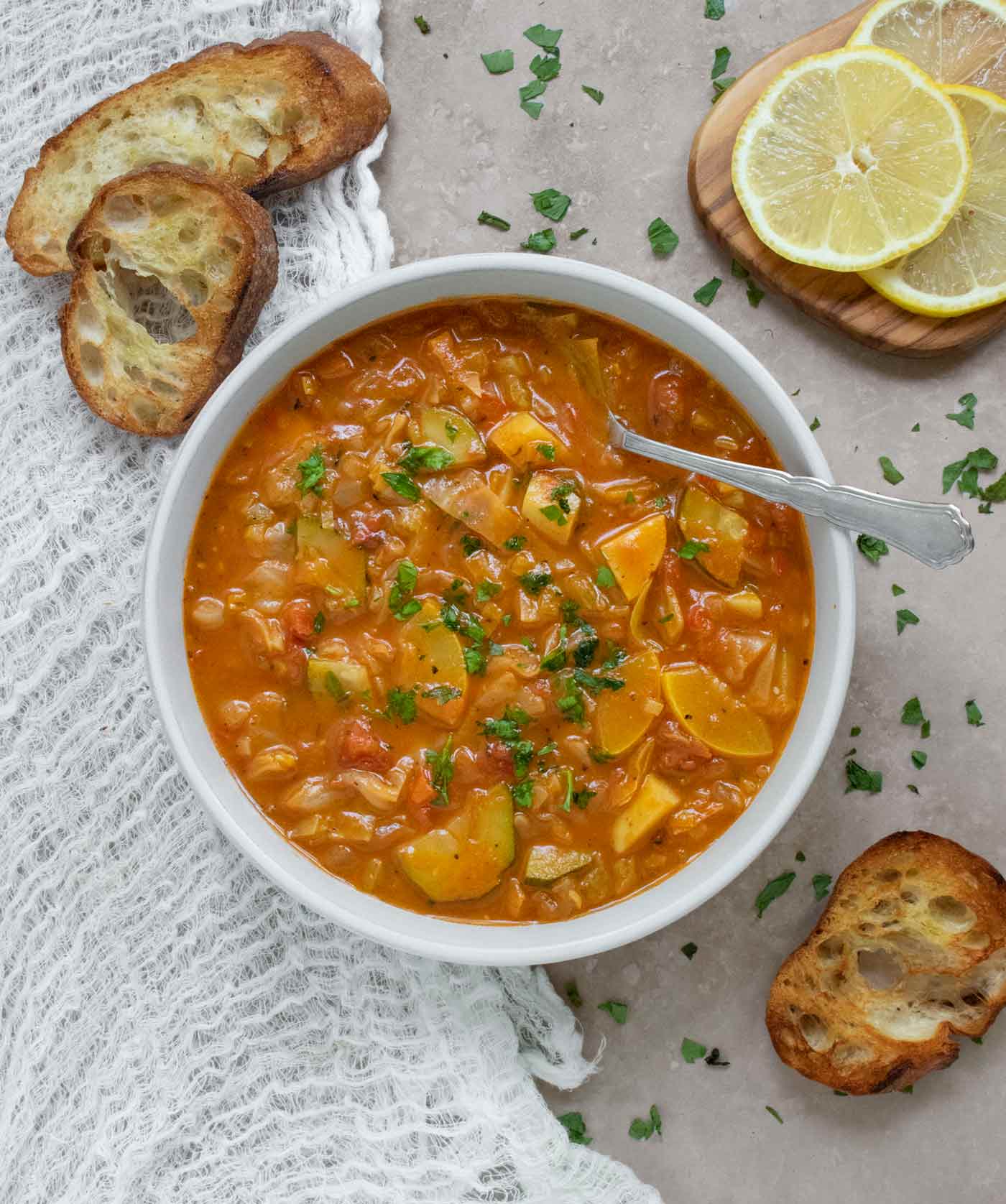 Overhead view of Summer Cabbage Soup in a bowl with a spoon, and sliced bread on the side.