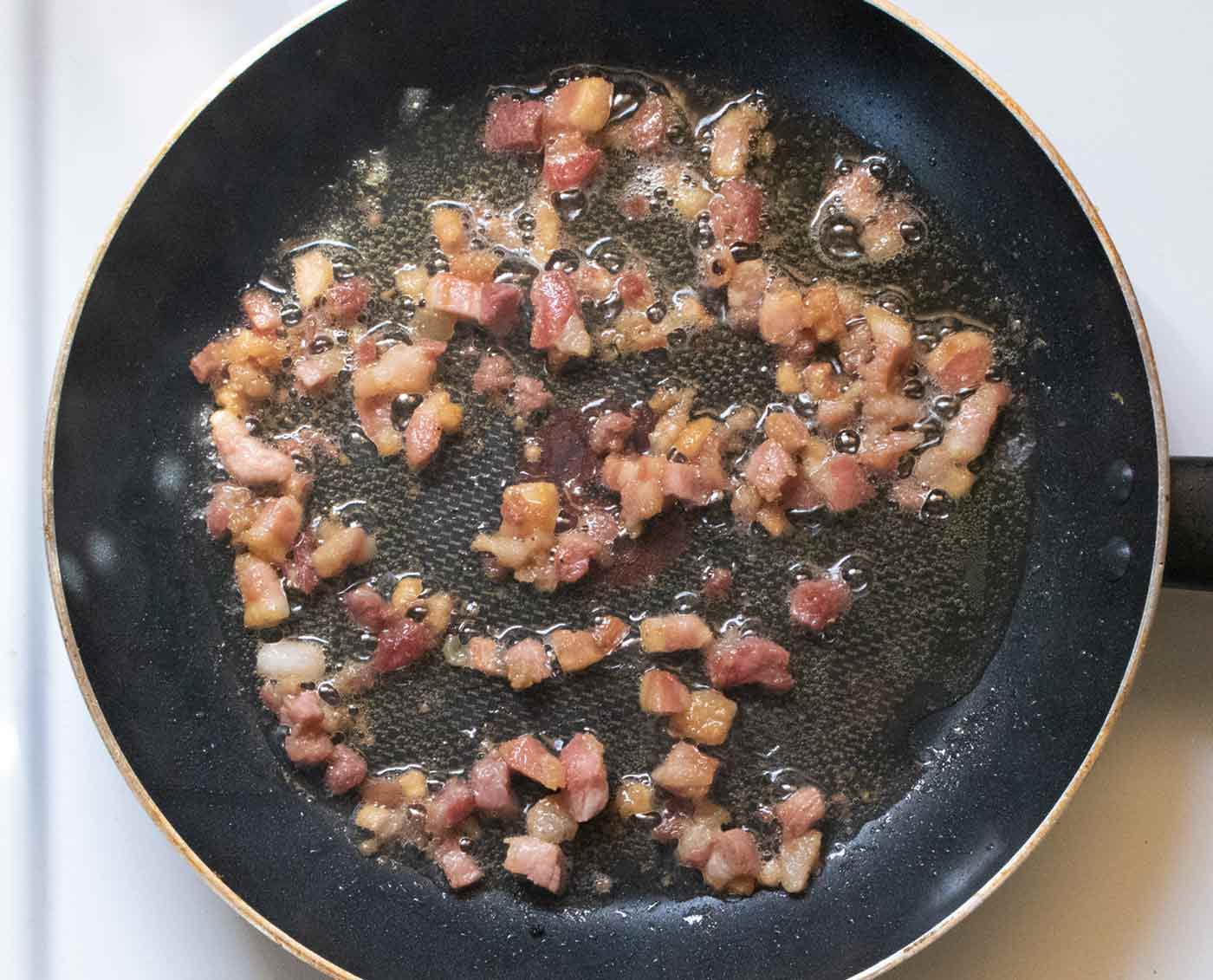 Small cubes of pancetta crisping in a non-stick skillet.
