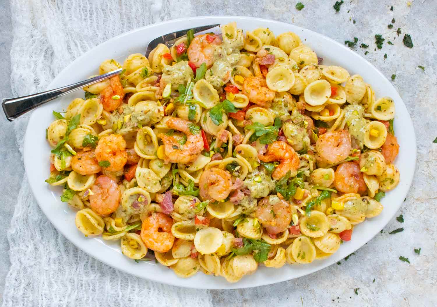 Summer Shrimp & Pancetta Pasta Salad on a white serving platter with a serving fork.
