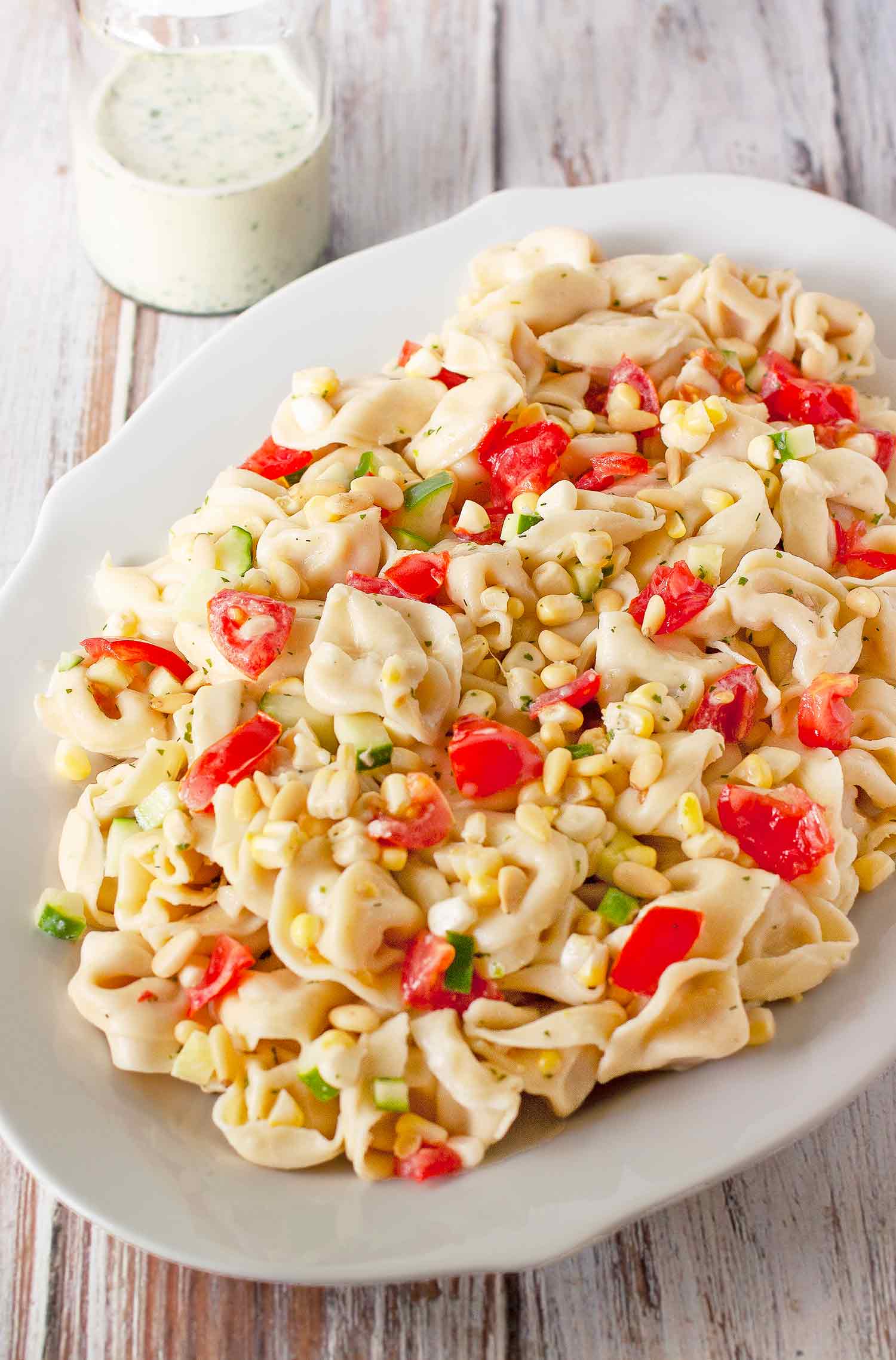 Summer Tortellini Pasta on a serving platter with a side of buttermilk dressing in a glass jar.