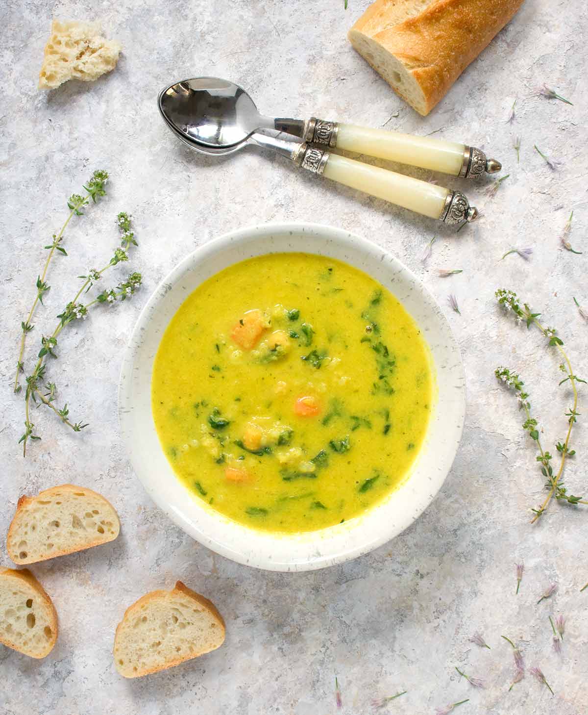 Bowl of soup with spoons and sliced bread to the side.