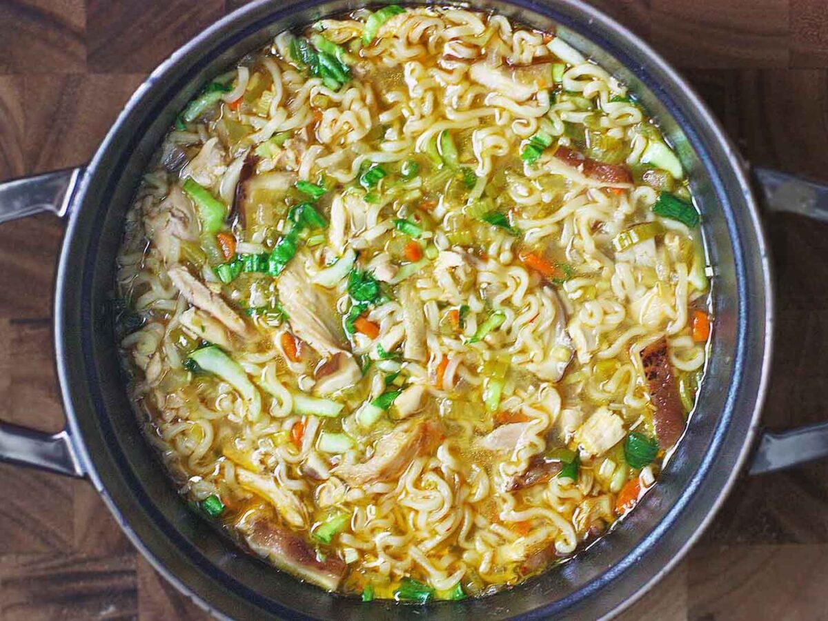 Thai Ramen Noodle Chicken Soup in a large black Dutch oven, sitting on a wooden board.