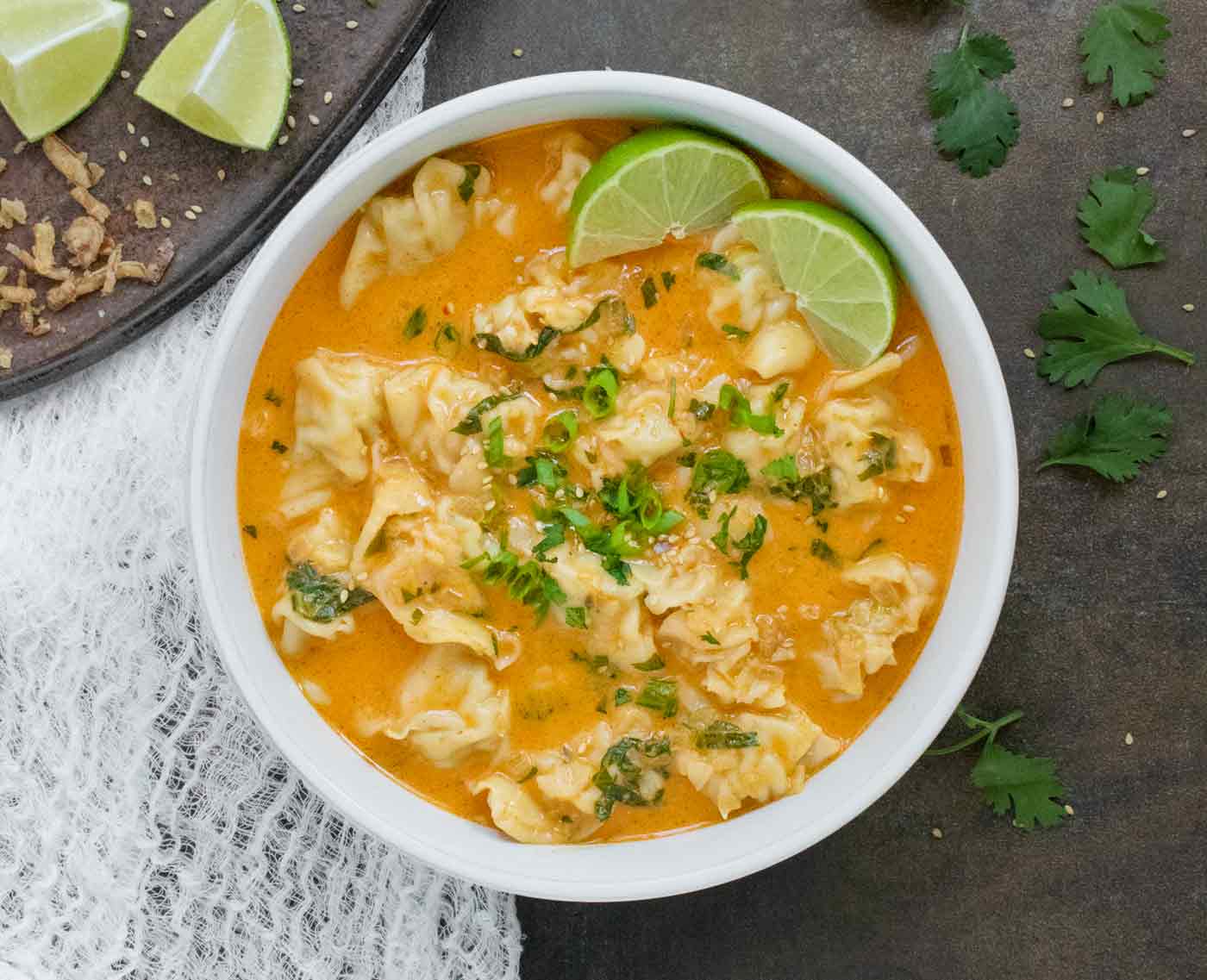 Overhead view of a bowl of Thai Red Curry Dumpling Soup with lime slices.