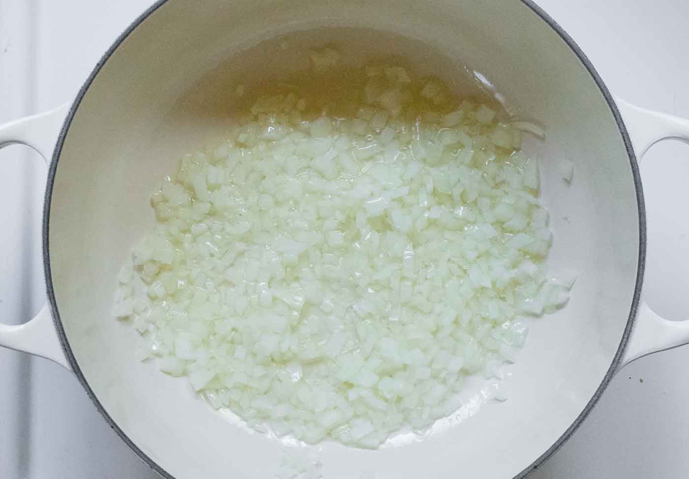 Onions sauteing in a white Dutch oven.