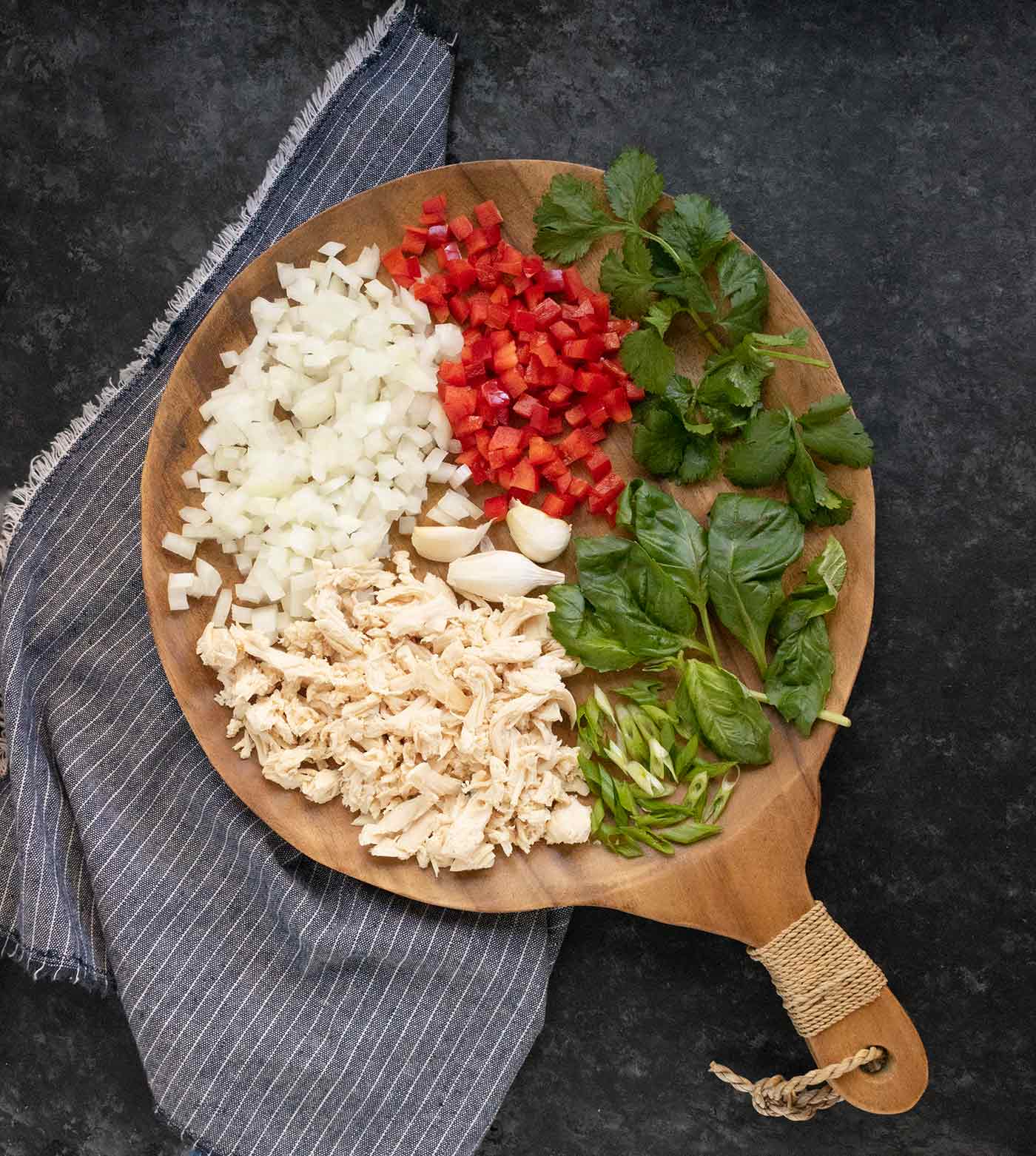 Aromatic ingredients chopped and arranged on a round wooden serving board.