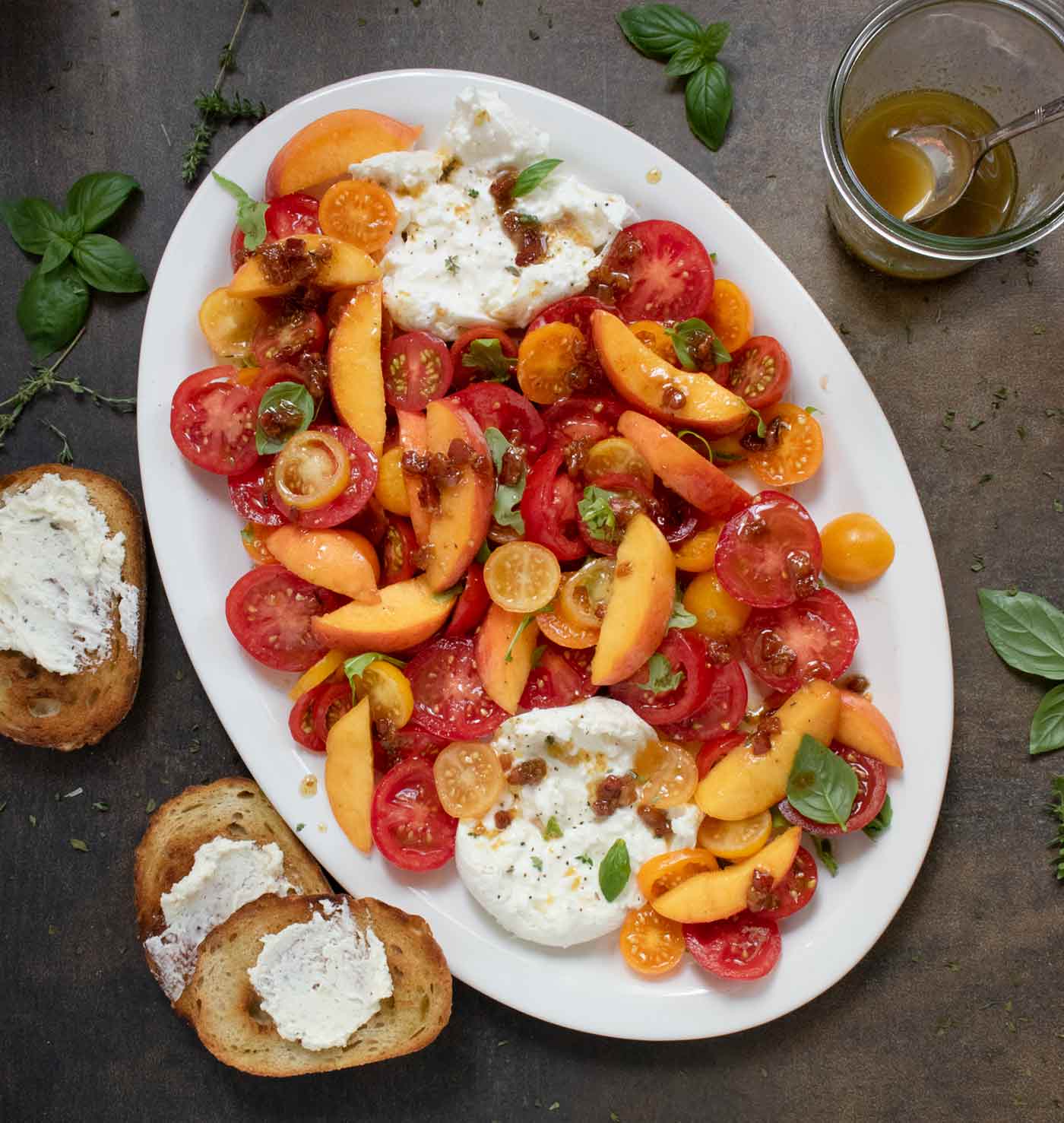 Tomato Peach Burrata Salad on a platter with the jar of bacon vinaigrette on the side.