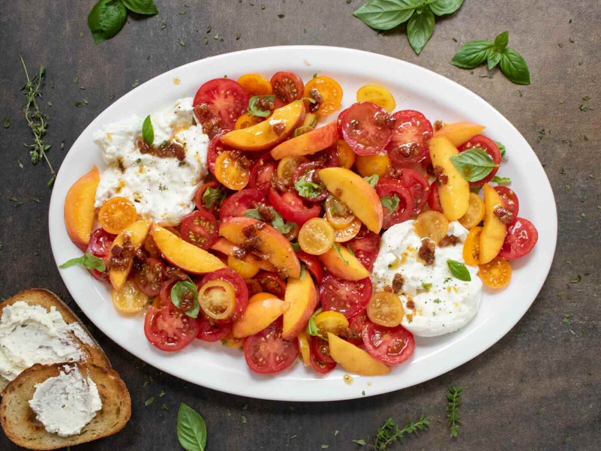 Overhead view of Tomato Peach Burrata Salad on an oval, white serving platter.