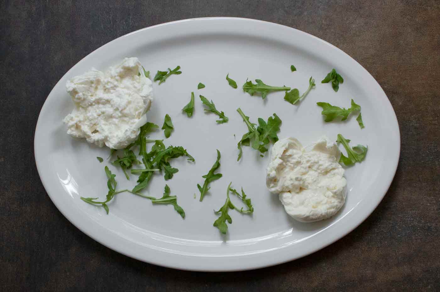 Arugula and burrata arranged on a white serving platter.