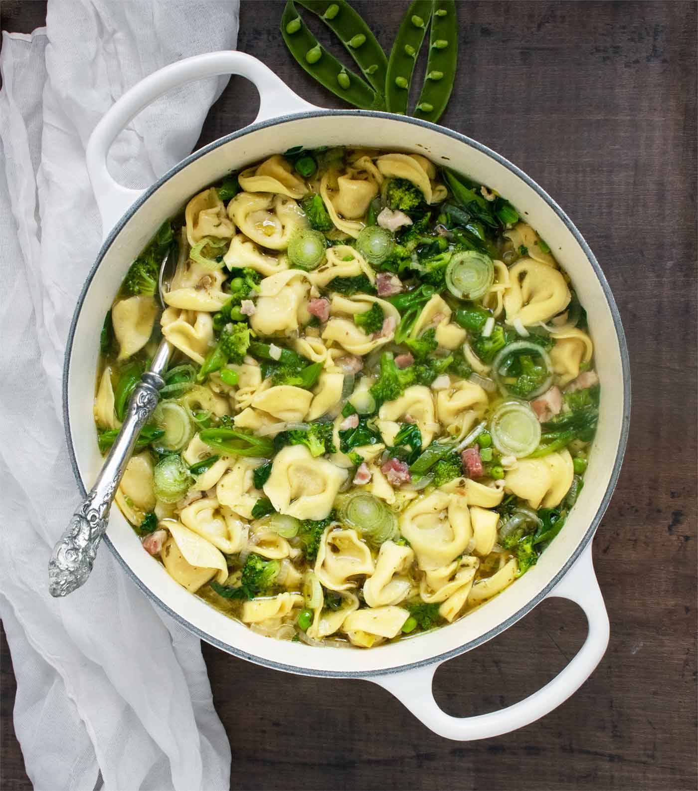 Overhead photo of Tortellini Primavera Soup in a white Dutch oven with a serving spoon.