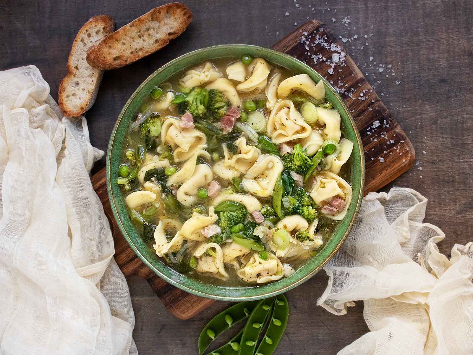 Photo taken from above of a bowl of Tortellini Primavera Soup on a wooden serving board.