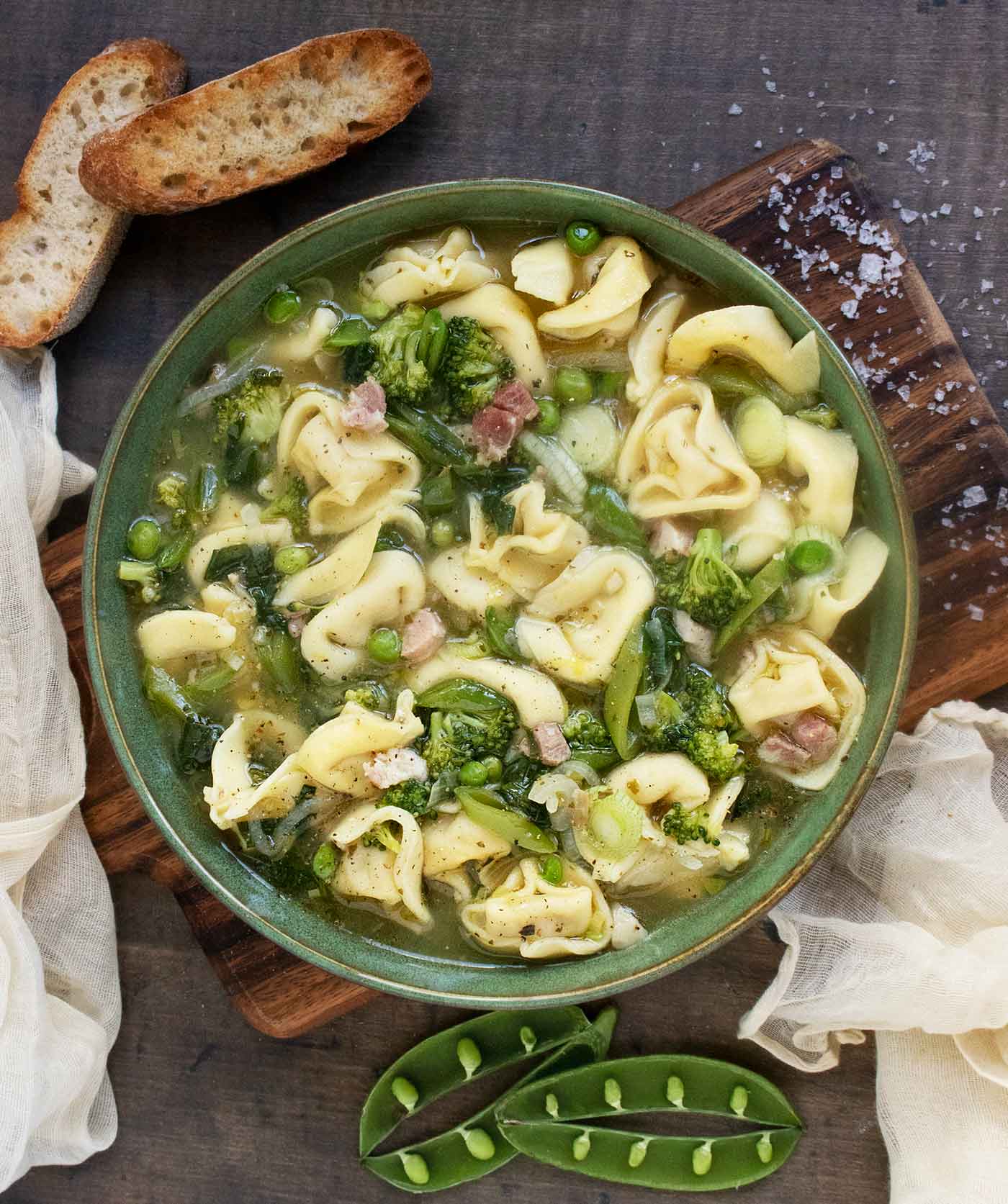 Photo from above of a bowl of Tortellini Primavera Soup with a side of bread.