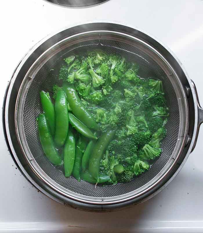 Broccoli and sugar snap peas blanching in boiling water.