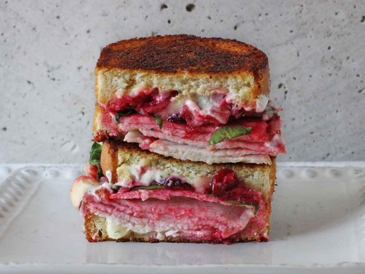 Turkey Cranberry Grilled Cheese sandwich sliced in half and stacked on a white plate.