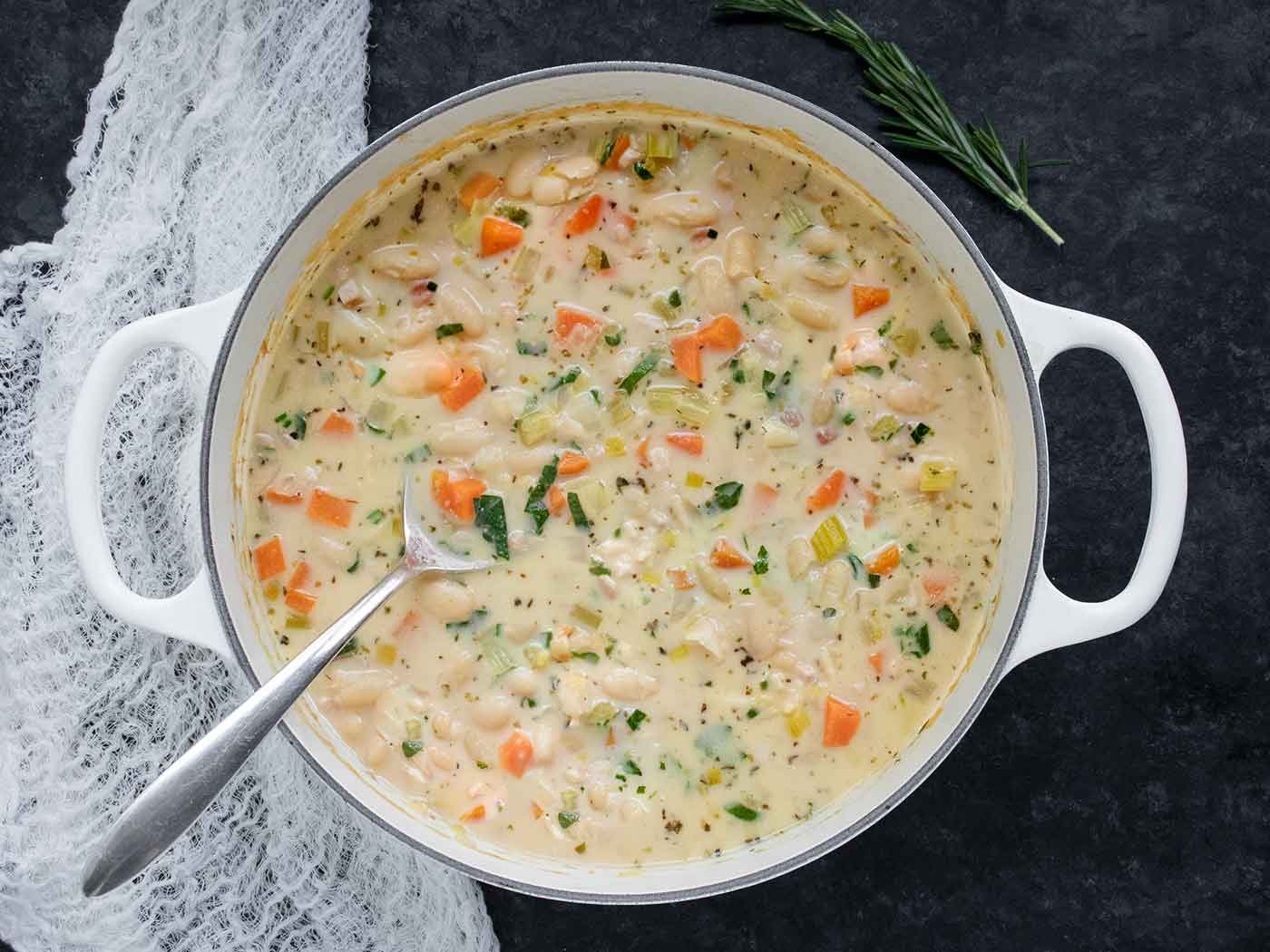 Overhead view of Tuscan White Bean Soup in a large white Dutch oven with a serving spoon.