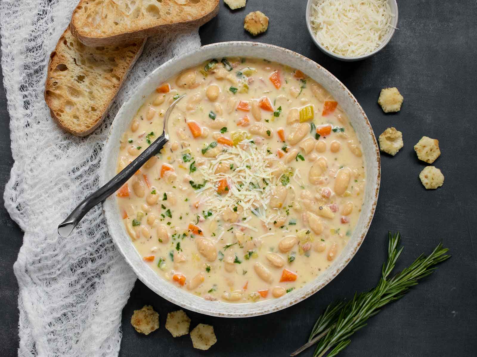 Overhead view of Tuscan White Bean Soup in a bowl with a spoon and a side of bread slices.