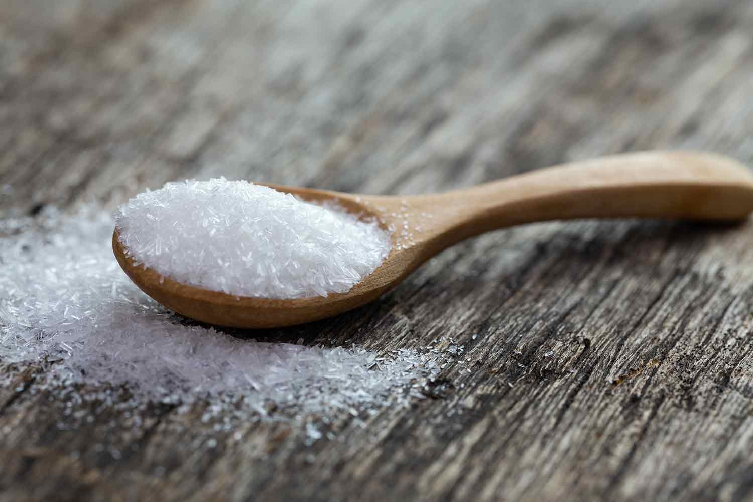 Crystalline MSG on a wooden spoon on a cutting board.