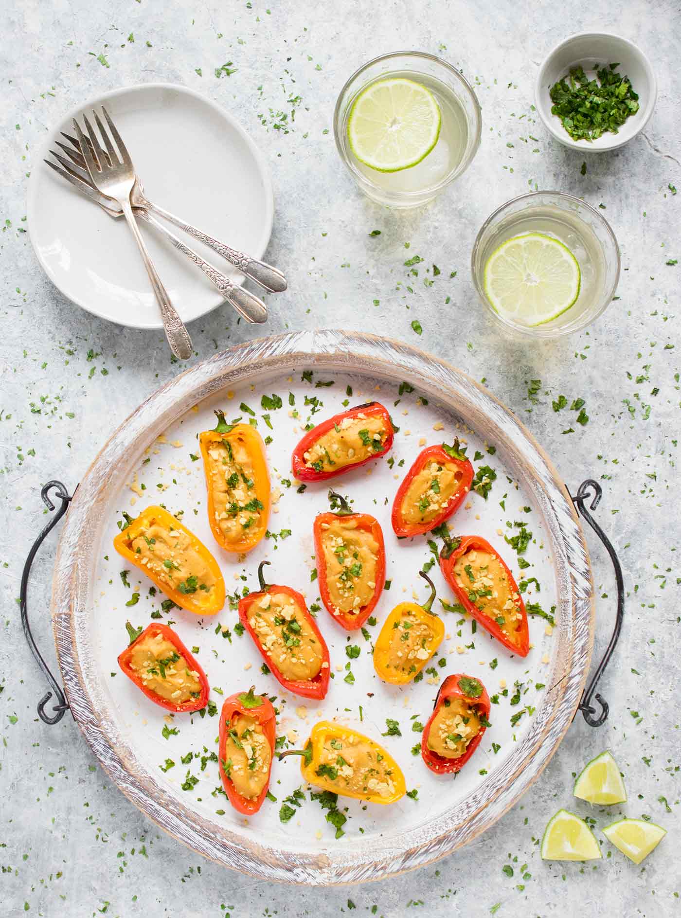 Vegan queso stuffed mini peppers on a large white serving tray, with margaritas