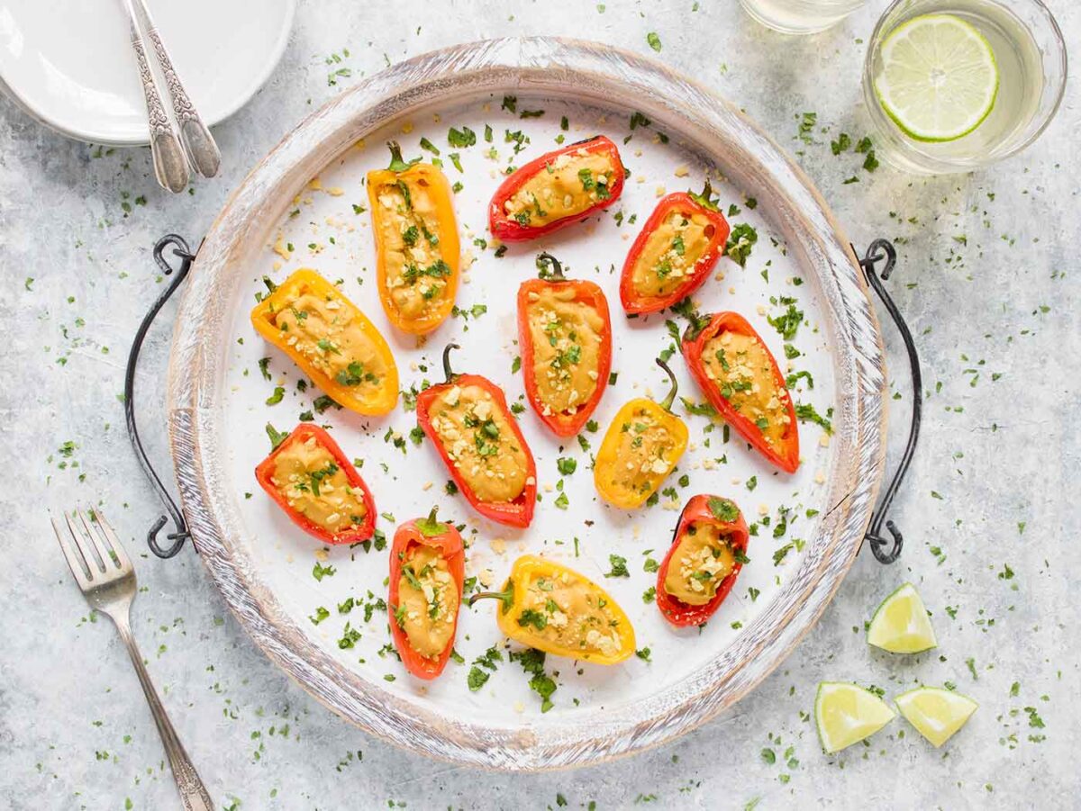 Vegan queso stuffed mini peppers on a white serving tray.