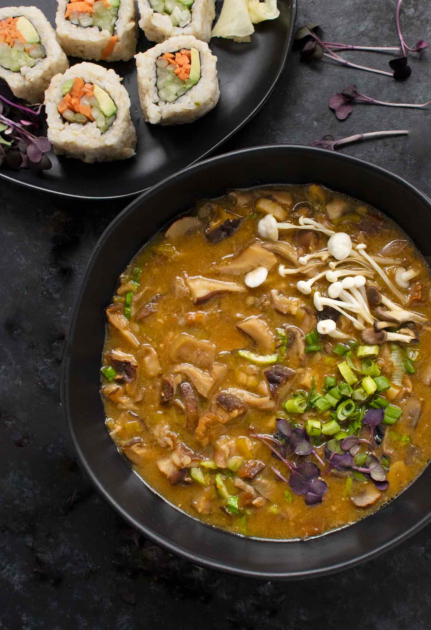 Wild Mushroom Miso Soup in a black bowl with a side of sushi.