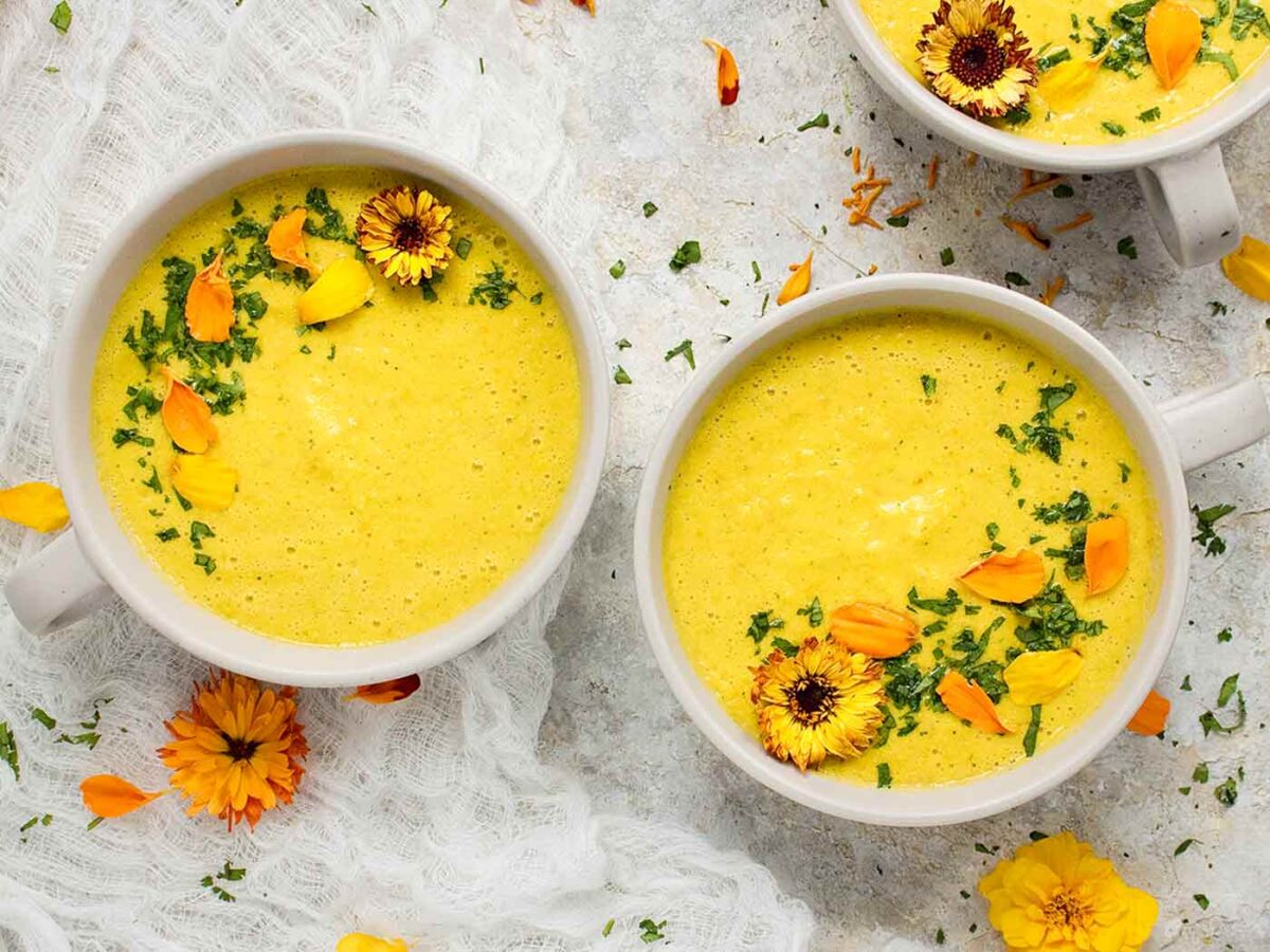 Overhead view of two bowls of Yellow Gazpacho, decorated with edible flowers in yellow and orange hues.