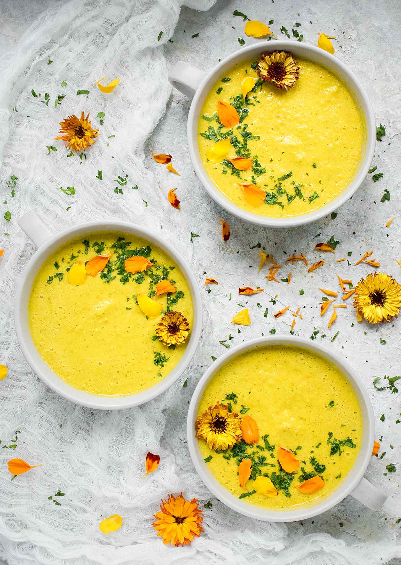 Three bowls of Yellow Gazpacho adorned with edible flowers
